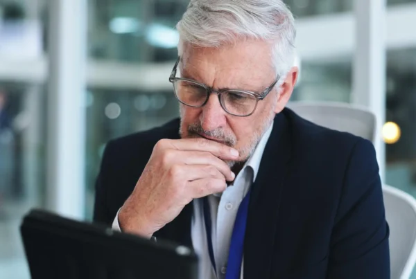 Empresario mayor con gafas, pensativo frente a una laptop en una oficina