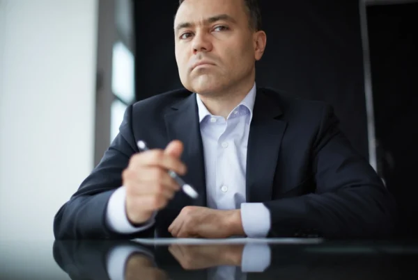 Hombre de negocios con traje sentado a la mesa, sosteniendo una pluma y con expresión pensativa