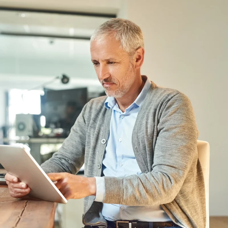 Hombre ejecutivo revisando información en una tablet en su oficina, analizando datos financieros relacionados con la validación fiscal de proveedores.