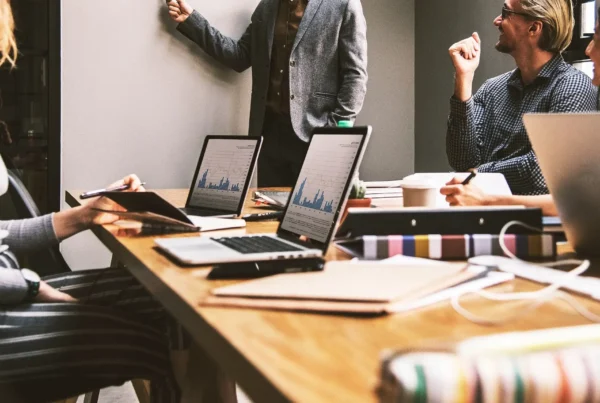 Equipo en sala de juntas revisa gráficas en laptops mientras un líder expone, representando modelos de análisis de sensibilidad para gestionar riesgo crediticio B2B.